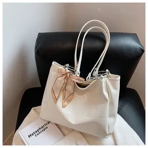 Detail of cream crocodile embossed tote bag with elegant silk scarf on leather sofa