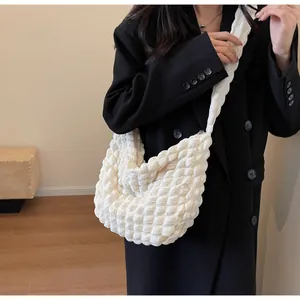 Détail du sac plissé blanc à texture pop-corn porté par un mannequin en blazer noir