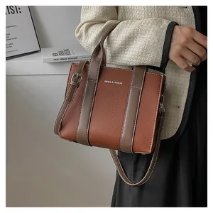 Detail of a brown lychee-textured tote bag with side metal buckles and white contrast stitching