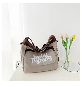 Vista dettagliata della borsa tote in tela beige con spalline marroni e scritte bianche sul davanti