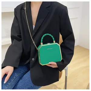 Detailed shot of green box clutch bag featuring gold trim and woven chain strap