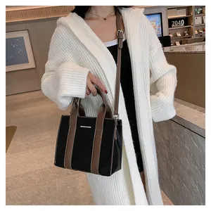 Black pebbled leather tote bag with brown straps styled on a white knit sweater