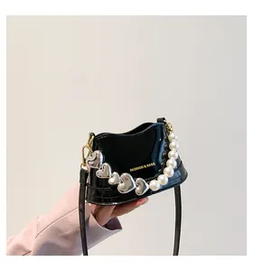 Dettaglio mini borsa in vernice nera con catena a cuore di perle e finiture dorate