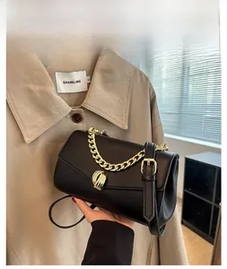 Detail of a black leather handbag featuring a gold chain handle and a spiral metal clasp