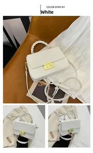 Close-up of white crossbody bag with gold lock and braided rope handle on brown leather chair