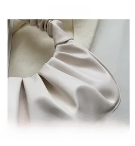 Close-up detail of pleated texture on a cream-white soft vegan leather shoulder bag