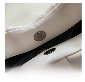 Detail of magnetic snap closure and leather pleats on a beige pleated shoulder bag