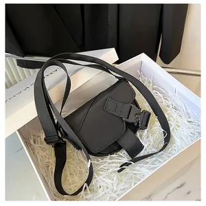 Dettaglio della borsa a sella in nylon nero con fibbia in una scatola regalo bianca