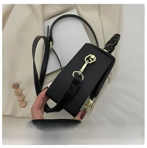 Detail of black box handbag with twisted rope handle and polished gold metal hardware