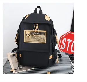 Dettaglio di uno zaino in tela nera con logo in pelle vintage appoggiato su una valigia
