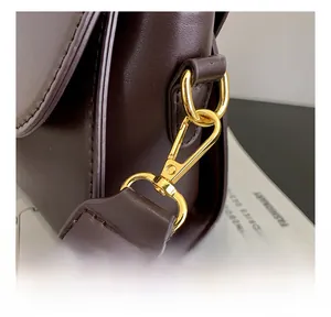 Close-up of golden metal swivel hook and stitching on dark brown leather shoulder bag