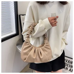 Detail showing pleated structure of beige ruched underarm bag on model with soft lighting