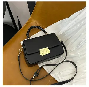 Detail of black structured crossbody bag featuring woven handle and gold metal clasp