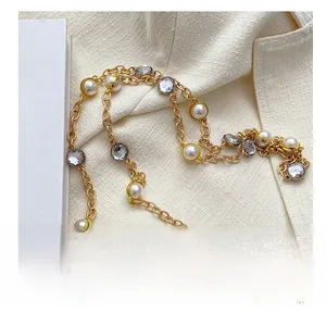 Detail of gold metal strap with white pearls and clear crystals on a textured fabric
