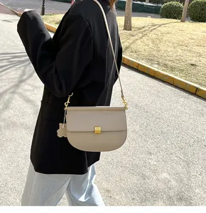 Dettaglio della borsa a sella beige con chiusura in metallo dorato e ciondolo a forma di orso
