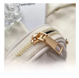 Macro shot of smooth gold zipper and V-quilted faux leather on white crossbody bag
