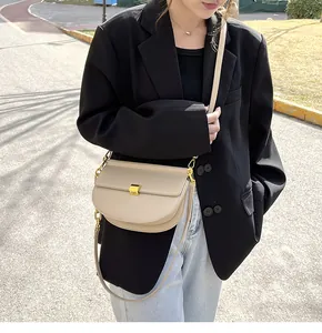 Dettaglio ravvicinato di una borsa a sella beige con fibbia in metallo dorato e pelle liscia