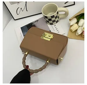 Close-up of brown leather square handbag with golden lock and twisted chain handle