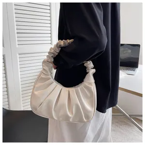 Detail of a beige pleated ruched hobo bag held by a model in a minimalist office setting