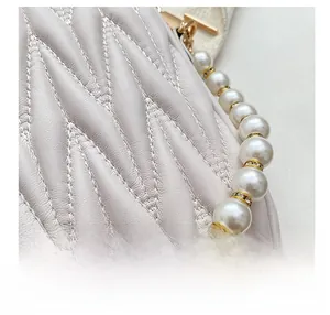 Detailed macro view of cream crossbody bag featuring leaf-pattern quilting and pearl handle