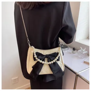 Dettaglio di borsa a tracolla bianco crema con grande fiocco nero e catena di perle