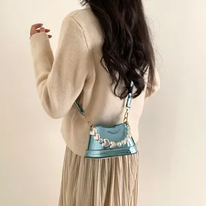 Mini borsa a secchiello in vernice celeste con manico di perle mostrata su una modella