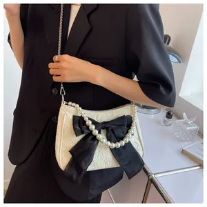 Dettaglio borsa bianca a trama con fiocco nero e manico di perle indossata da modella