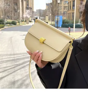 Dettaglio borsa a sella in pelle beige con fibbia dorata spazzolata in un contesto urbano