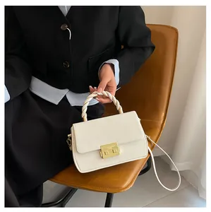 Close-up of a white leather crossbody bag with golden buckle and woven handle detail