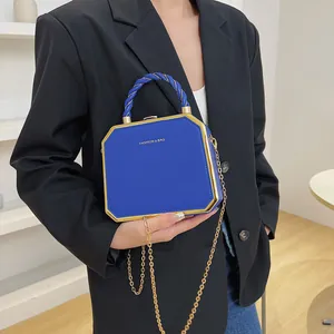 Blue octagonal acrylic box bag with gold trim and chain strap held by a model