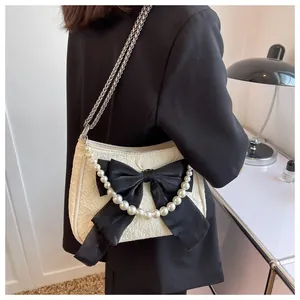 Dettaglio della trama, del fiocco nero e della catena di perle sulla borsa crema chic