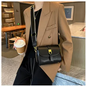 Detail of black leather crossbody bag with golden buckle and woven shoulder strap