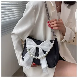 Dettaglio borsa nera in tessuto con grande fiocco bianco, catena di perle e tracolla