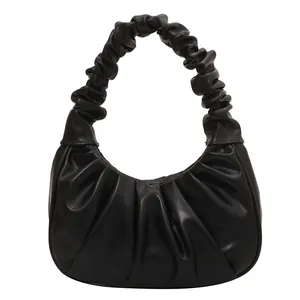 Detail view of the black ruched handle and pleated leather texture on this crescent bag