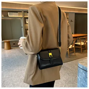 Close-up of black leather crossbody bag with yellow metal buckle and wide bicolor strap