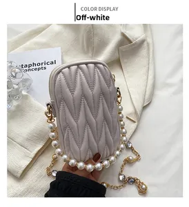 Detail of off-white quilted crossbody bag with pearl strap and rhinestone chain on blazer