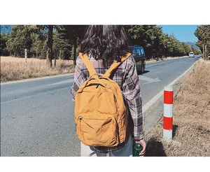 Vista posteriore all'aperto di uno zaino in tela gialla per donna in una foresta soleggiata