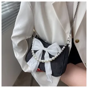 Dettaglio della borsa a tracolla nera testurizzata con fiocco bianco e perle eleganti