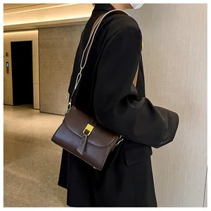 Detail of dark brown leather crossbody bag with gold buckle and woven strap on model