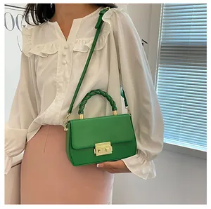 Detail of bright green crossbody bag with woven handle and gold clasp on a model