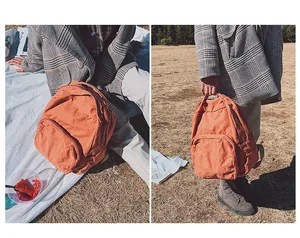 Dettaglio dello zaino vintage in tela arancione con doppia cerniera e manico su erba