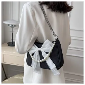 Dettaglio borsa a tracolla nera con fiocco in organza bianca, catena di perle e metallo