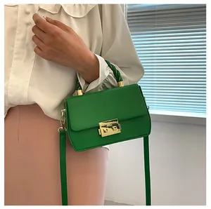 Detail shot of a vibrant green crossbody bag featuring a twisted handle and gold buckle