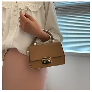 Detail of tan square handbag with woven handle and gold clasp on a model outfit