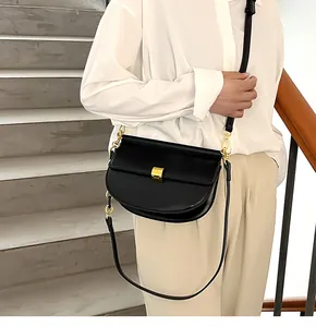 Modella che indossa una borsa a sella nera semicircolare con dettagli dorati su scale