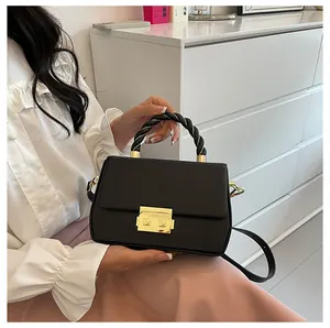 Detail of black crossbody bag with twisted rope handle and gold metal lock on matte leather