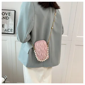 Detail of pink quilted phone bag with pearl handle and metal chain on a gray blazer