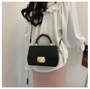 Detail of black crossbody bag with woven gold-tone handle and elegant metal clasp