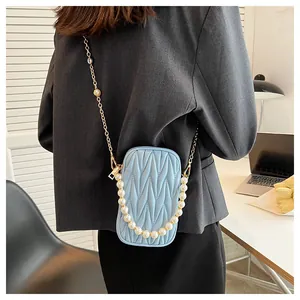 Close-up of light blue quilted phone bag with gold chain and pearl strap on model