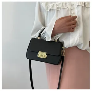 Detail of black rectangular crossbody bag with golden clasp and twisted top handle strap